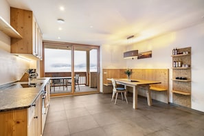 Una cucina moderna con mobili in legno, un'area pranzo con tavolo e sedie, e una vista tramite una porta in vetro.