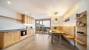 Une cuisine moderne avec des meubles en bois, un coin repas comprenant une table et des chaises, et une vue à travers une porte vitrée.