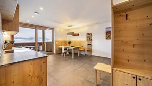 Une cuisine moderne avec des meubles en bois, un coin repas comprenant une table et des chaises, et une grande fenêtre offrant une vue sur les montagnes.