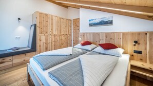 A bedroom with a wooden headboard, a bed with multiple pillows, a bench with a book, and a wall-mounted picture.