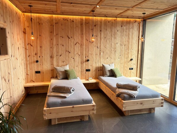 A room with two wooden beds, a bench, and a large window.