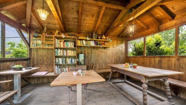 Un intérieur rustique en bois, avec une table centrale, des étagères et une vue sur la verdure à l’extérieur.