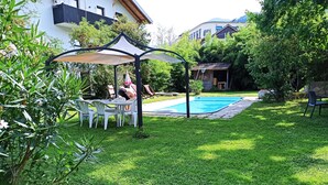 Un jardin avec une piscine, un espace salon couvert et une pelouse.