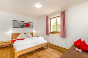 Une chambre à coucher avec un lit en bois, une fenêtre avec des rideaux, une table de chevet et un luminaire fixé au mur.