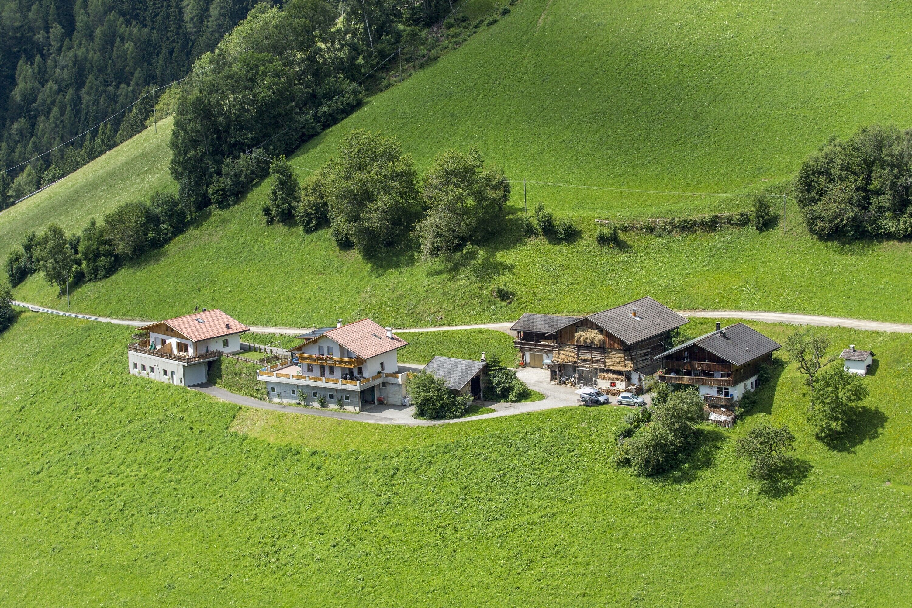 Una propiedad en una ladera con varias construcciones, un camino pavimentado y campos verdes circundantes.