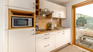 A modern kitchen with a built-in microwave, wooden shelves, and a view of a deck through a glass door. - Apartment 'Tratterhof Apt Eidechsspitze' with Mountain View, Private Terrace and Wi-Fi (Vandoies)
