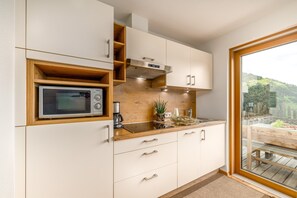 A modern kitchen with a built-in microwave, wooden shelves, and a view of a deck through a glass door.