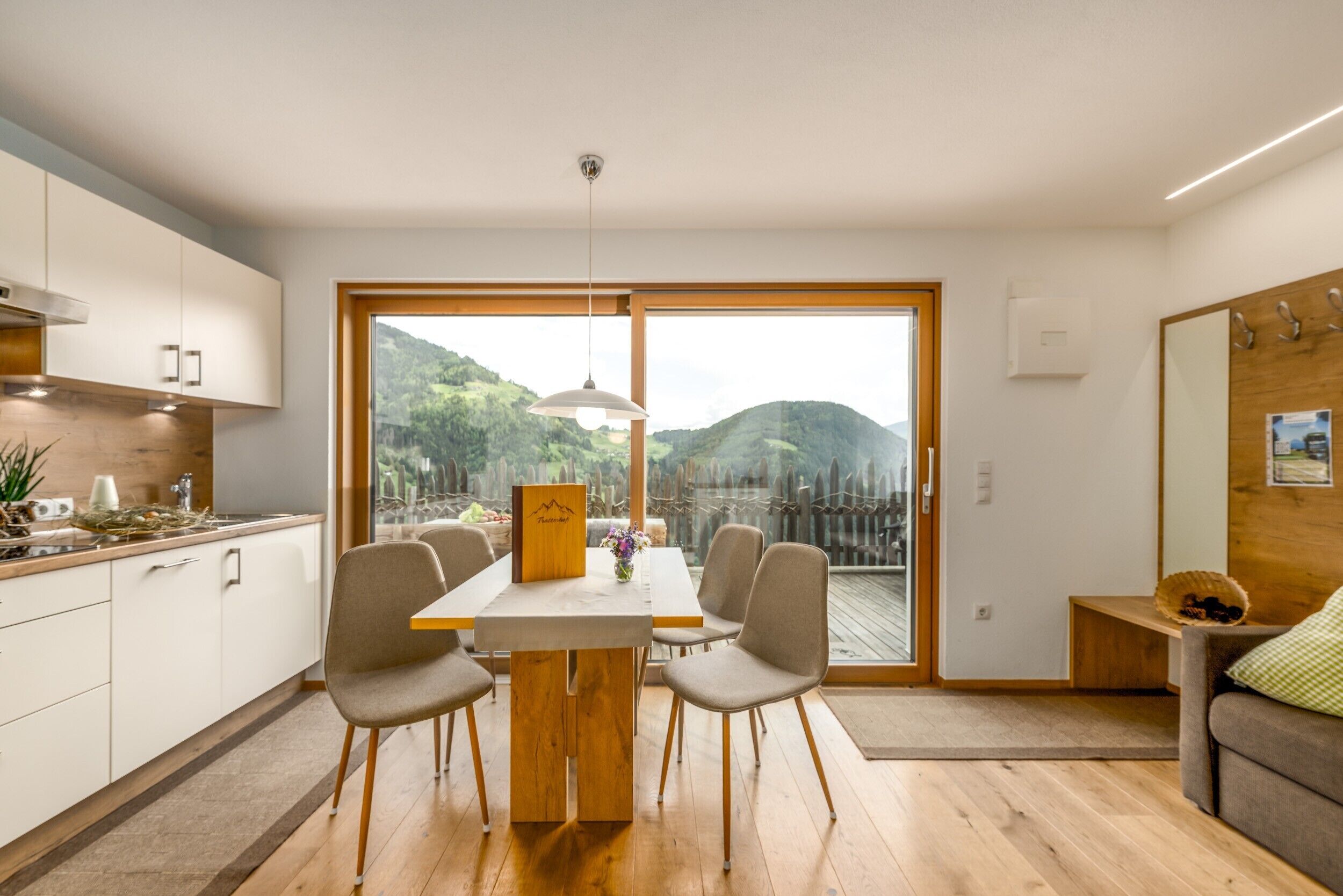 A modern kitchen with a dining table and chairs, a view of the outdoors, and a wooden bench in the living area.