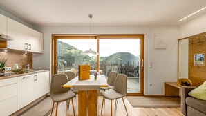 A modern kitchen with a dining table and chairs, a view of the outdoors, and a wooden bench in the living area. - Apartment 'Tratterhof Apt Eidechsspitze' with Mountain View, Private Terrace and Wi-Fi (Vandoies)