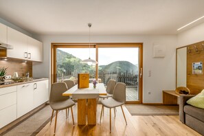 A modern kitchen with a dining table and chairs, a view of the outdoors, and a wooden bench in the living area.