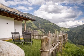 Un chalet entouré d’une clôture en bois, avec deux chaises et une vue sur un paysage montagneux.