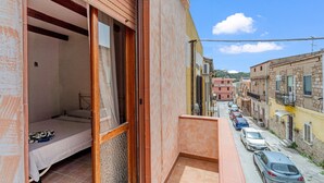 A narrow street with parked cars, a building with a balcony, and a bed in a room. - Apartment 'Casa Rustica' with Private Terrace, Wi-Fi and Air Conditioning (Gonnesa)