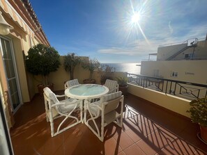 Un balcon avec une table ronde et des chaises, des plantes en pot et une vue sur la mer.