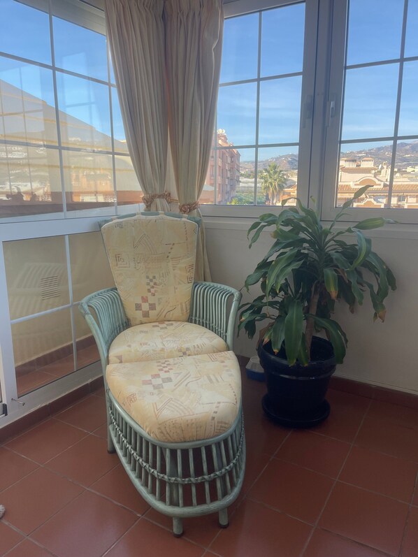 Un balcón con una silla de mimbre, una planta en maceta y vistas de edificios.