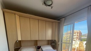 Habitación de hotel con una cama grande, cabecera de madera, una lámpara de techo y vistas a edificios a través de la ventana.