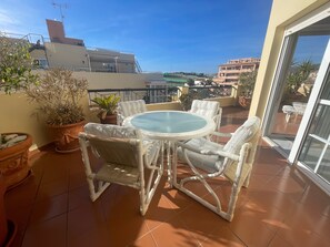 Un balcon avec une table ronde et des chaises en osier, des plantes en pot et une vue sur les immebles.