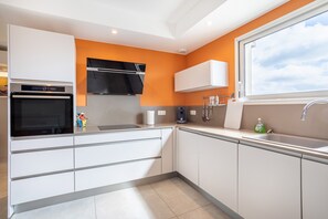 A modern kitchen with white cabinets, a built-in oven, a black range hood, a window with a view, and a sink with a faucet.