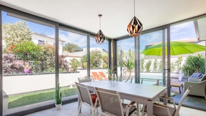 Un comedor con mesa y sillas, ventanas amplias y vistas a una piscina y jardín.