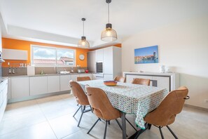 A modern kitchen with white cabinets, a dining table with a patterned tablecloth, and two pendant lights.