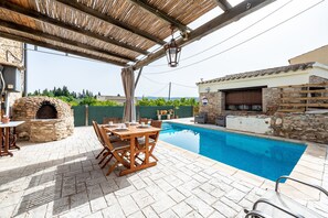A poolside area with a stone oven, wooden table, and chairs.
