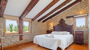 Un dormitorio con pared de piedra, vigas de madera, una cama, una mesita de noche y una ventana con vistas.
