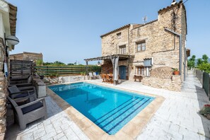 A stone building with a swimming pool, outdoor furniture, and a pergola.