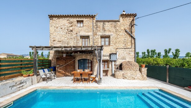 Un edificio de piedra con piscina, mobiliario exterior y una pérgola.