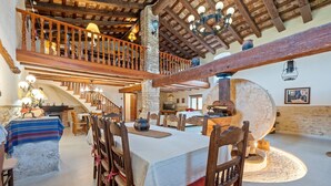 Un interior rústico con vigas de madera a la vista, una chimenea de piedra y un comedor con sillas y una mesa de madera.