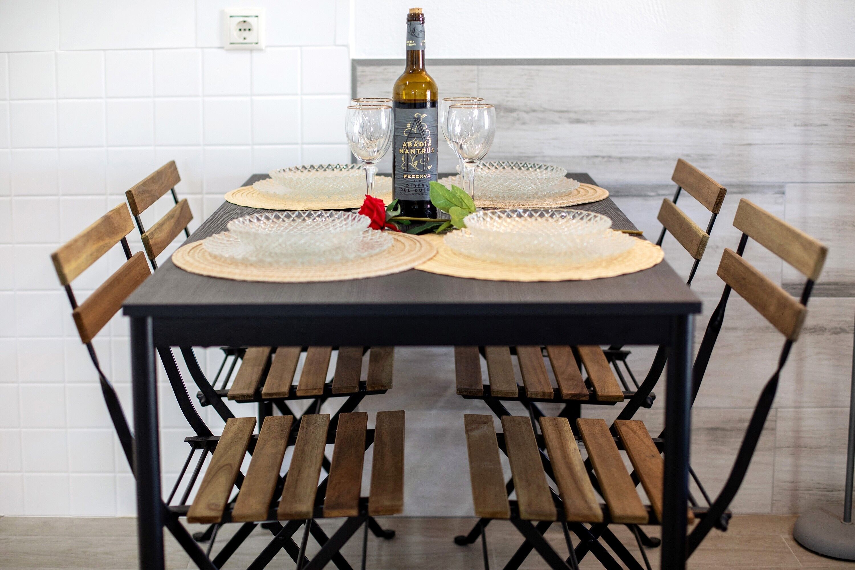 A dining table with a bottle, glasses, and a red rose centerpiece.