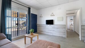 A modern living room with a sofa, a small table with a plant, a TV mounted on the wall, and a view through large sliding doors to an outdoor area. - Casa la Viña with pool, Wi-Fi, and air conditioning (Chiclana de la Frontera)