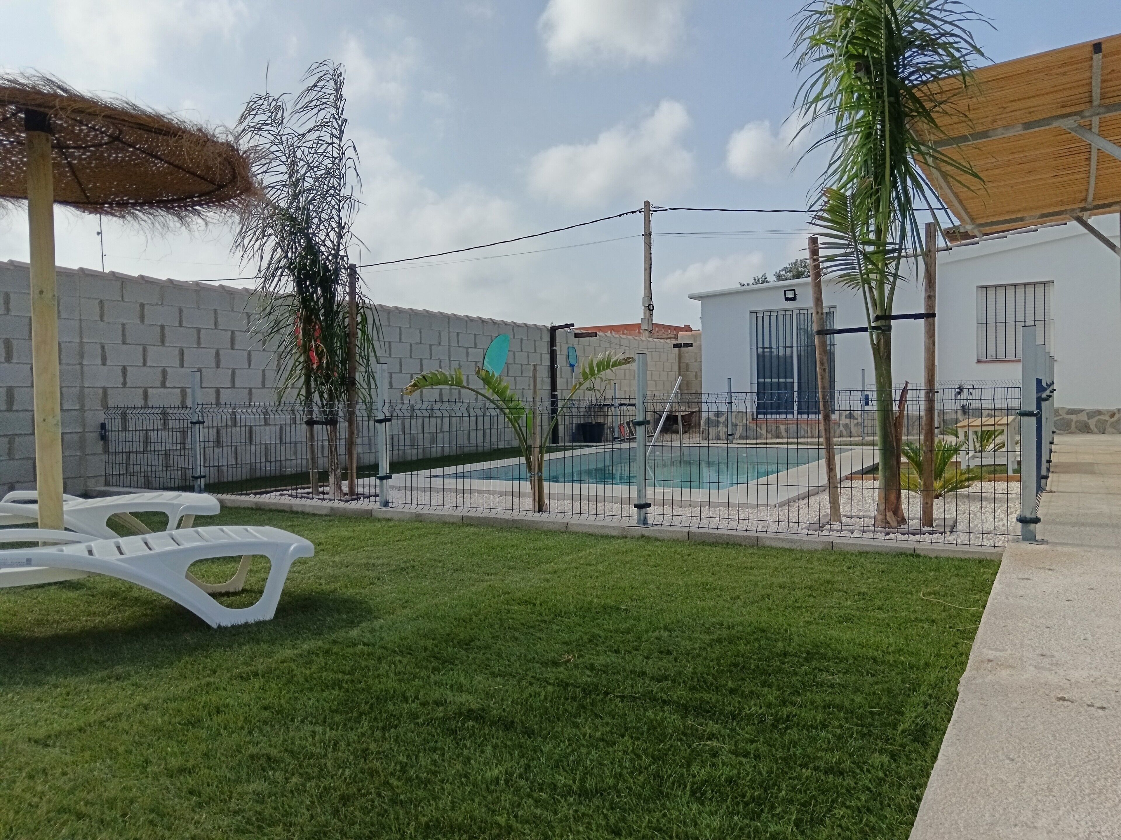 Patio trasero cercado con piscina, césped y edificio blanco con ventana.