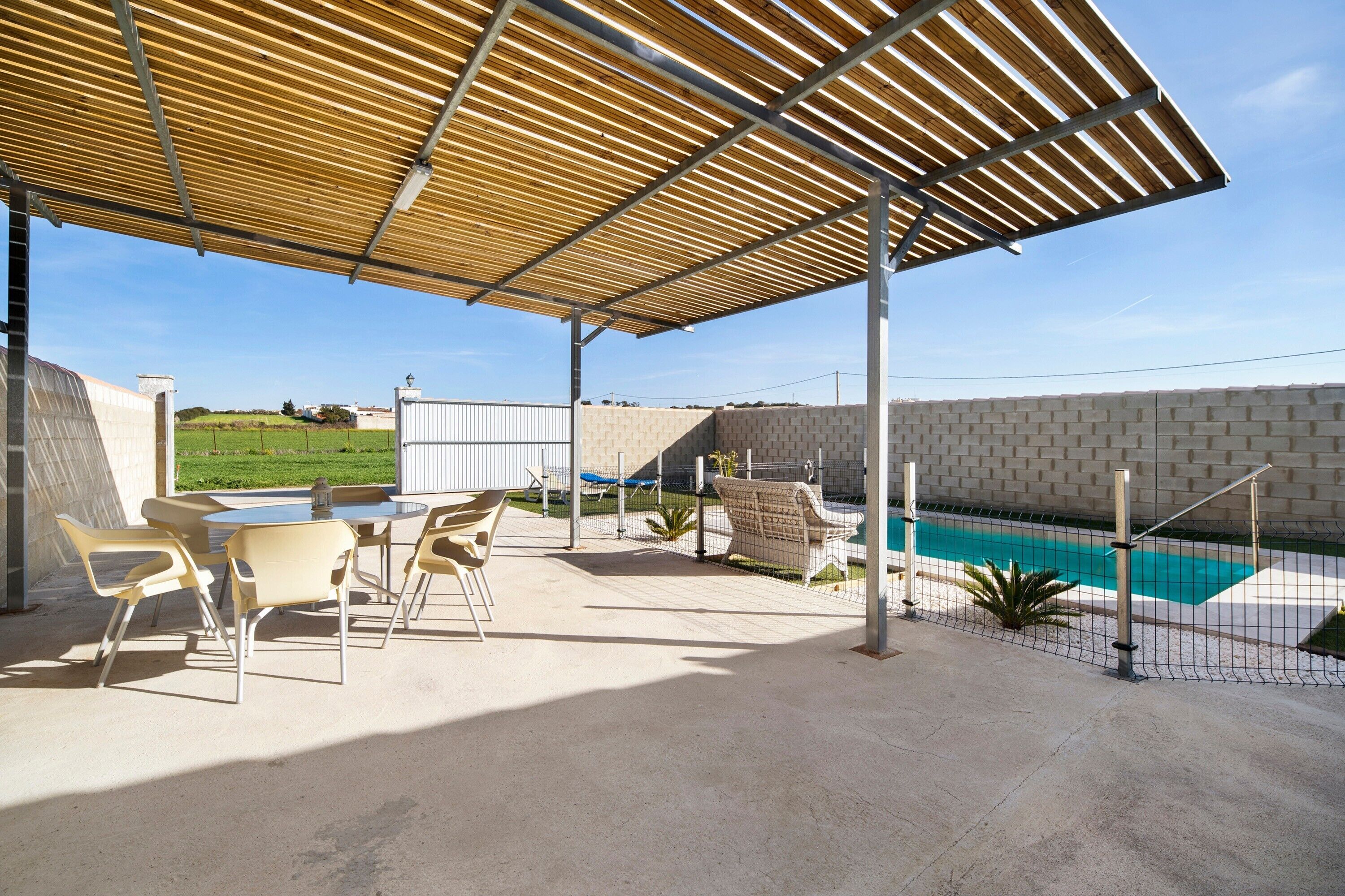 A covered patio with outdoor furniture, a swimming pool, and a brick wall.