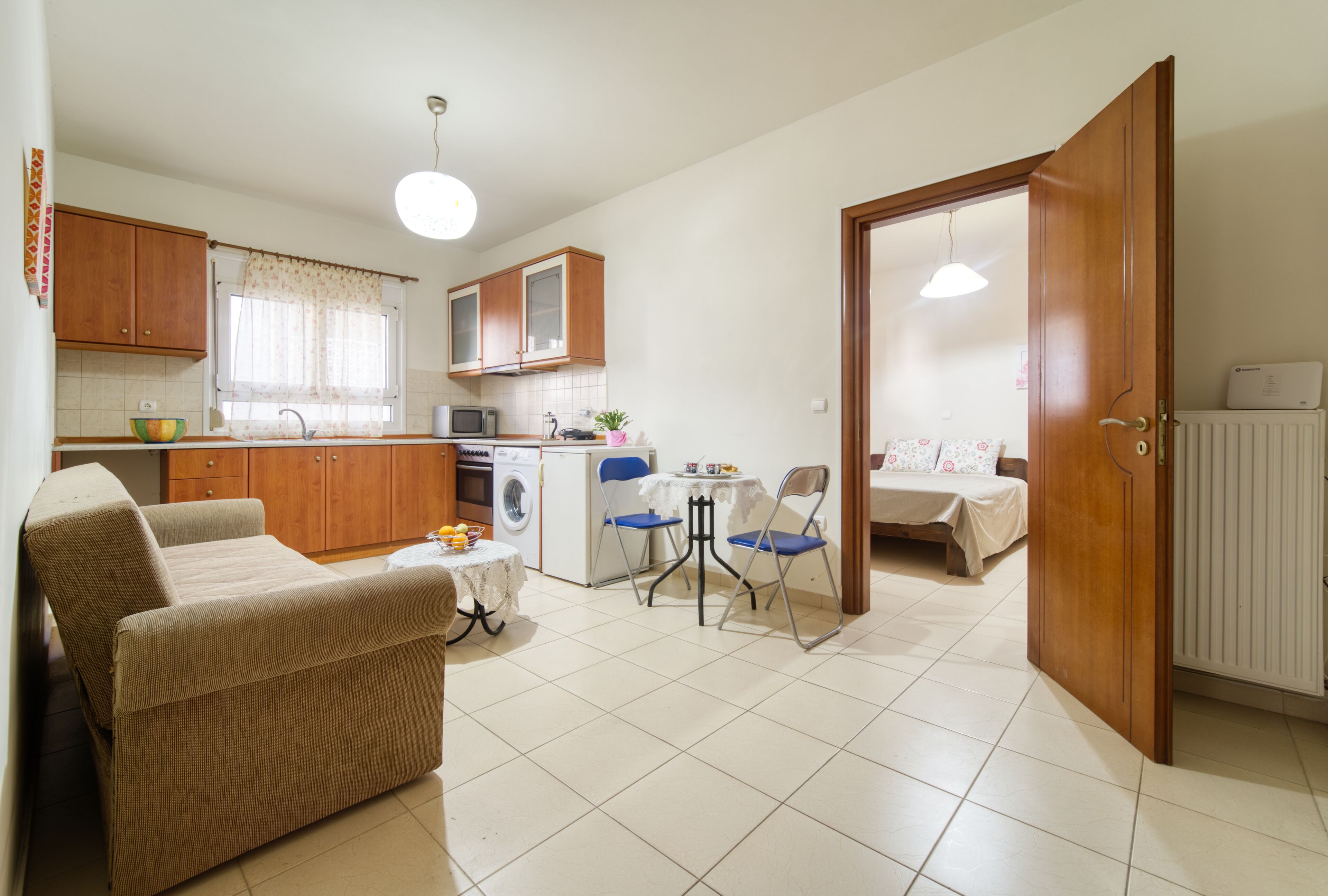 Ein kompakter Wohnraum mit einer Küchenzeile, einem Essbereich mit einer Couch und Stühlen sowie einem Schlafzimmer mit einem Bett und einem Nachttisch.