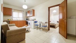 A compact living space with a kitchenette, a dining area with a sofa and chairs, and a bedroom with a bed and a nightstand. - ParkApart Rhodes Town (Rhodes)