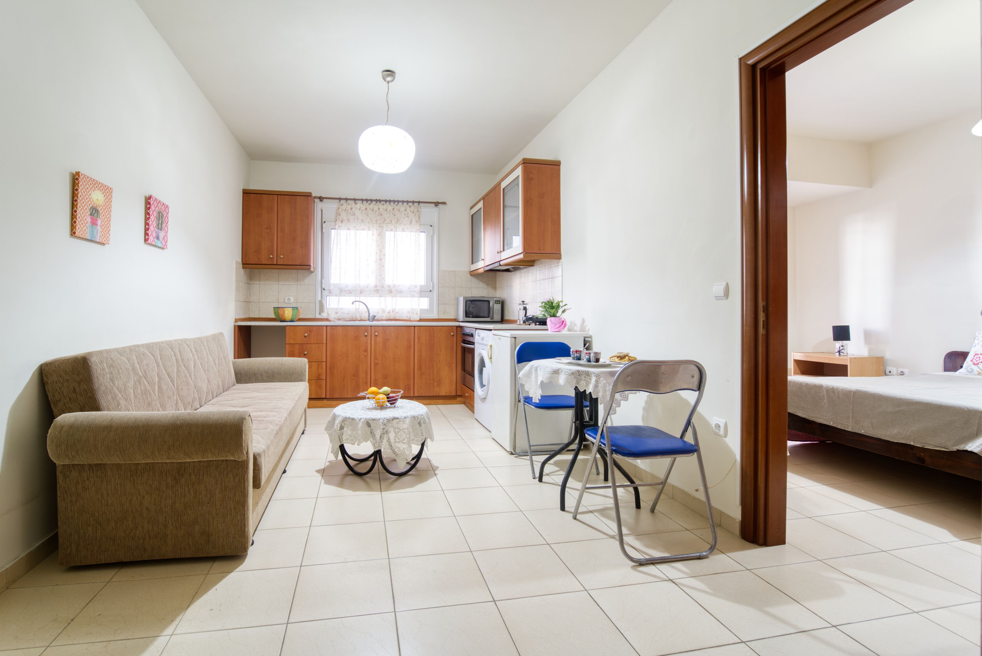 A compact living space with a sofa, a dining table with chairs, a kitchen area with cabinets and appliances, and a bed in the adjacent room.