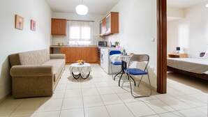 A compact living space with a sofa, a dining table with chairs, a kitchen area with cabinets and appliances, and a bed in the adjacent room. - ParkApart Rhodes Town (Rhodes)