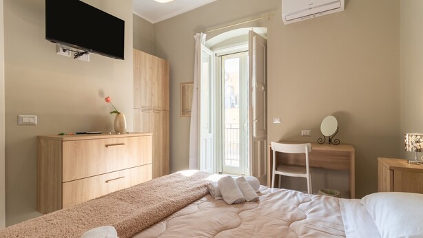 A bedroom with a bed, a desk, a chair, a TV, and an air conditioning unit.