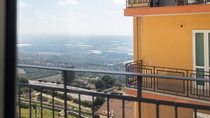 A balcony with a view of a distant landscape, a yellow building, and a metal railing.