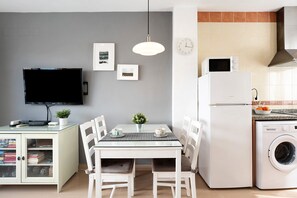Une cuisine compacte équipée d’un four à micro-ondes, d’un lave-linge et d’un téléviseur à écran plat fixé au mur.
