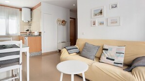 A living room with a beige sofa, a small round table, and a white chair. There is a kitchen area with a countertop and a microwave. - Family Only Holiday Apartment "Manuela" with Sea View, Shared Terrace & Wi-Fi (CONIL DE LA FRONTERA)