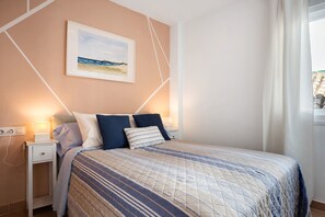 Une chambre à coucher comprenant un lit, des tables de chevet, une commode, un tableau accroché au mur et une fenêtre avec des rideaux.