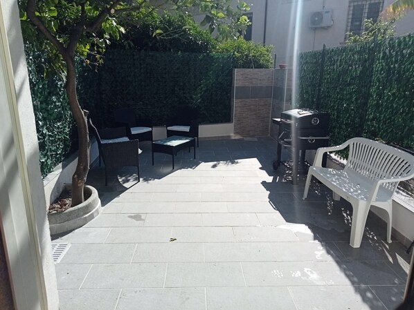 Un patio con una parrilla, un banco de plástico blanco y una mesa con sillas.