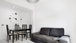 Een moderne eethoek met een klok aan de muur, een eettafel met stoelen en een grijze bank.