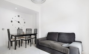 Ein moderner Essbereich mit einer Uhr an der Wand, einem Esstisch mit Stühlen und einem grauen Sofa.