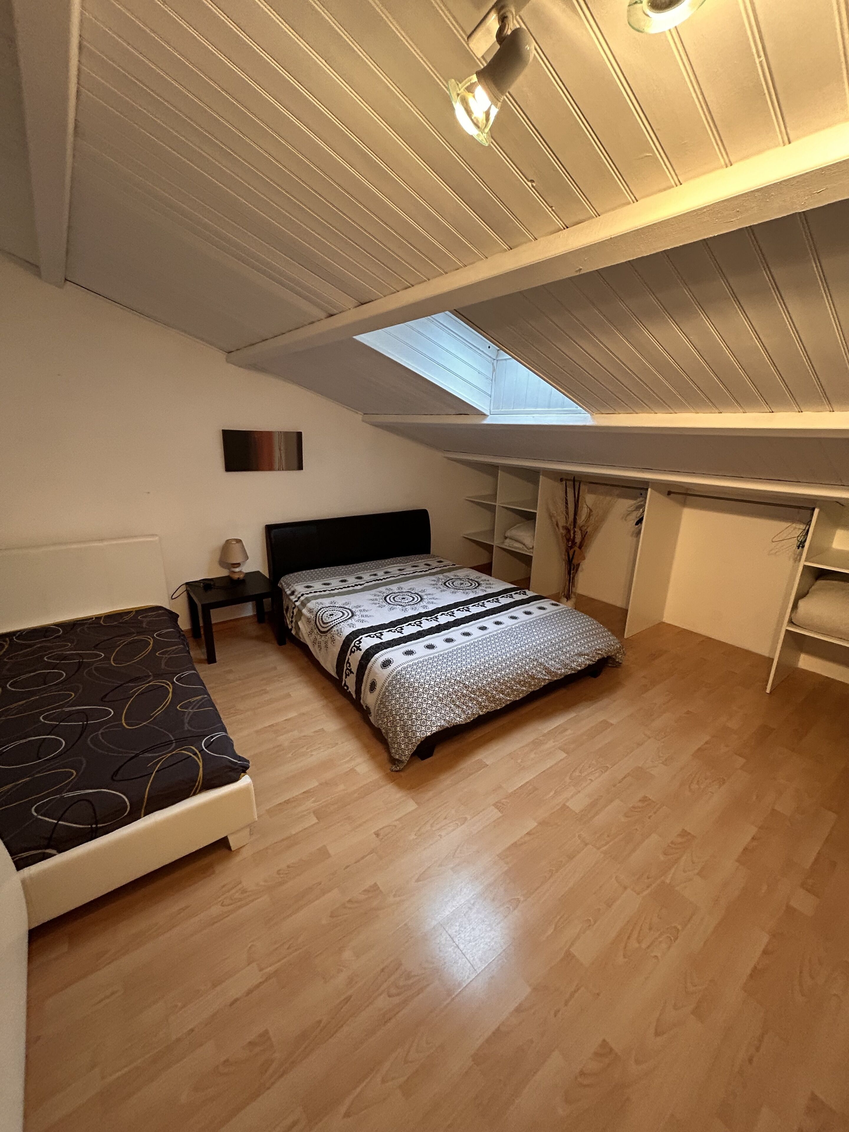 Een slaapkamer met dakraam, een bed met beddengoed met patroon, een nachtkastje en een bureau met stoel.