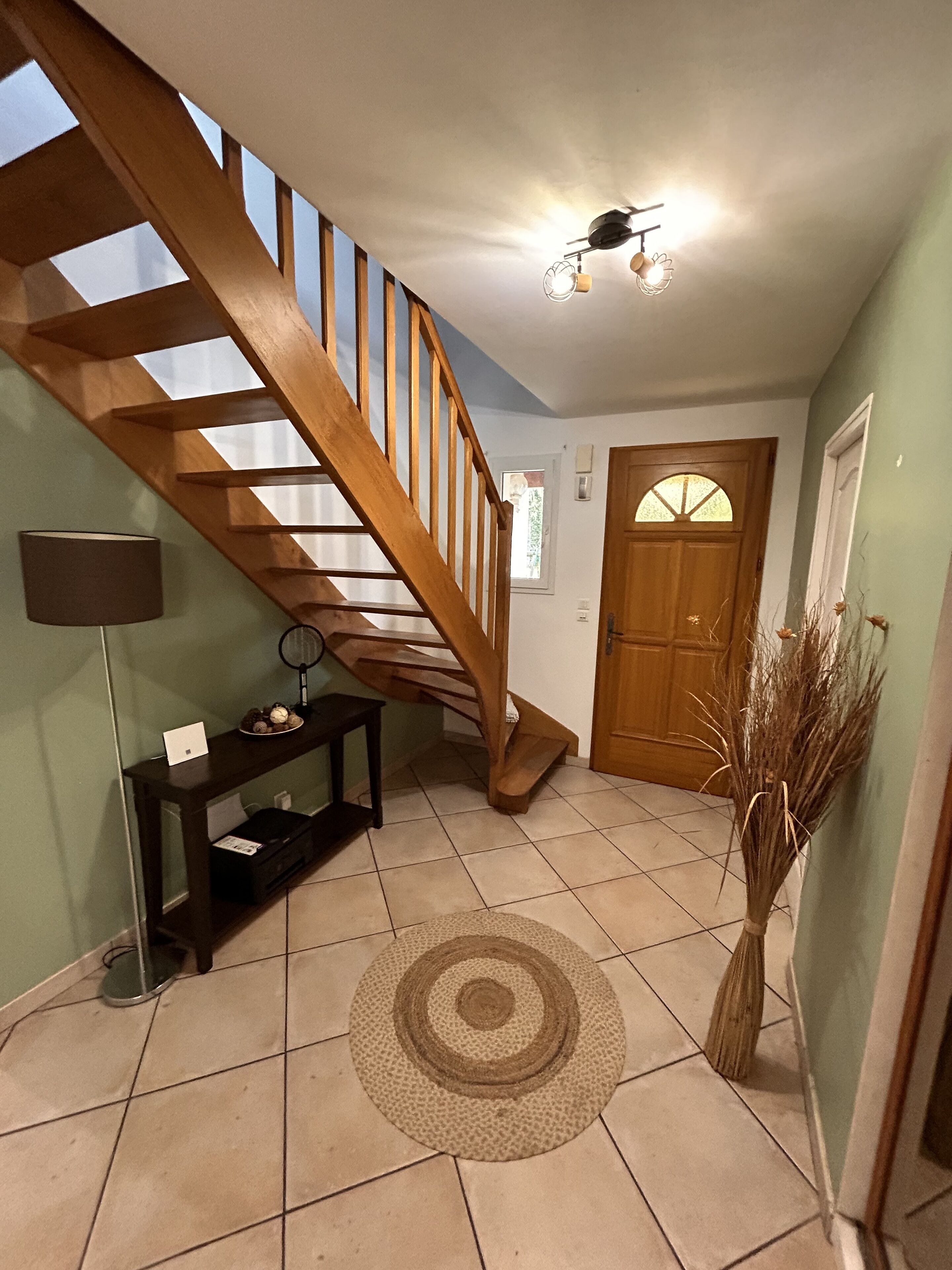 Eine Treppe mit Holzwangen führt zu einer oberen Etage, eine Tür mit Glasfenster, ein kleiner Konsolentisch mit Lampe und ein dekorativer Teppich auf dem Boden.