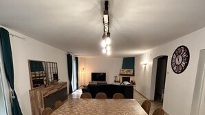 A dining area with a large table, chairs, a television, and a clock on the wall.