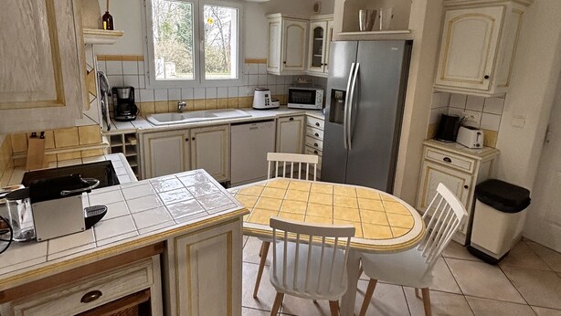 A compact kitchen with a central island, white cabinetry, and a dining table with chairs.