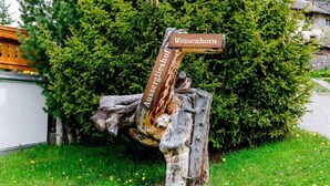 Puisesta kyltistä on kaiverrettu teksti »Weisenhorn», ja se on sijoitettu vehreän kasvillisuuden ja rakennuksen taustalle.