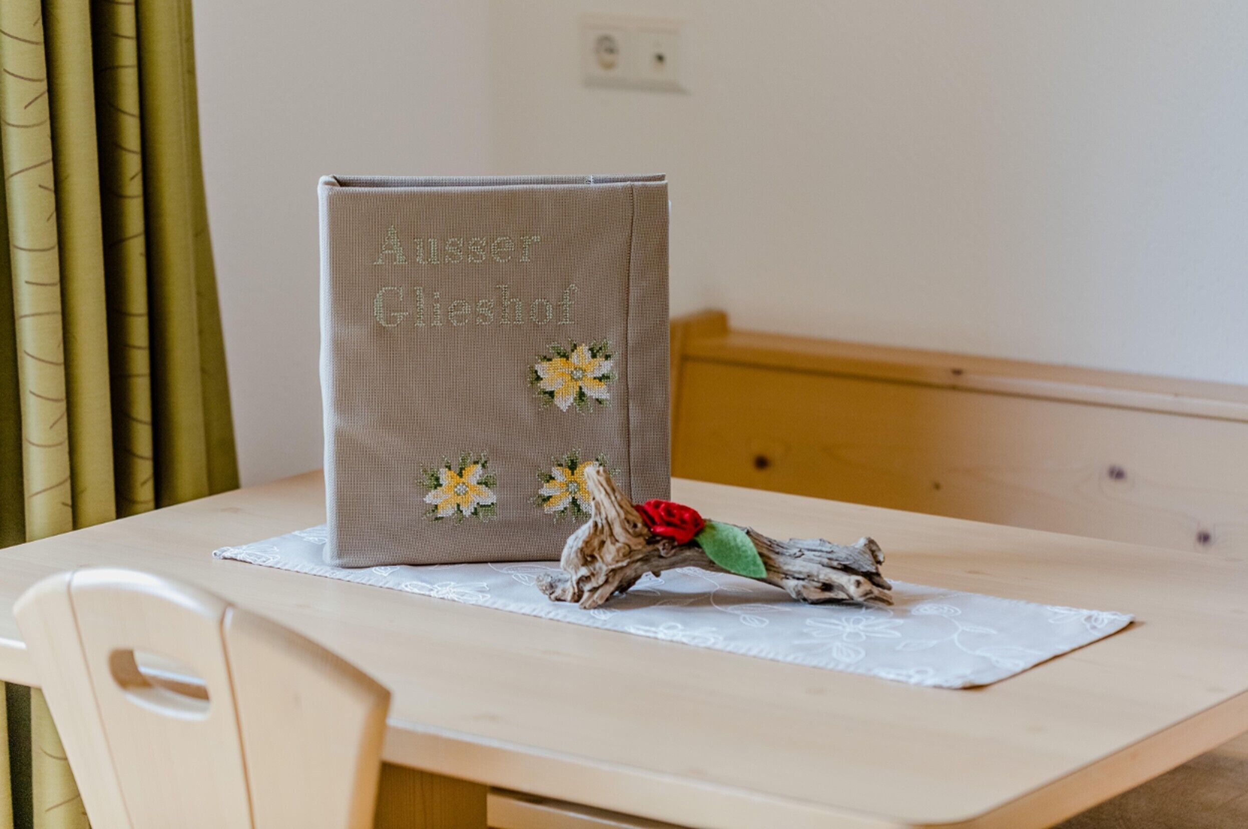 Une table sur laquelle se trouve un livre intitulé « Aussers Gieshof » et une branche décorative ornée d’une fleur rouge.